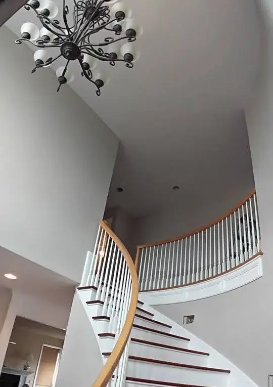 Interior painting project: two-story foyer with a curved staircase, white balusters, wood handrail, and wrought-iron chandelier